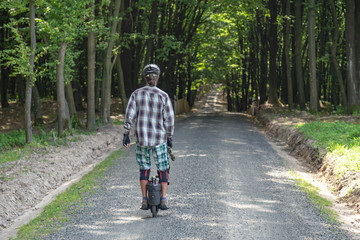 Men in protective wear riding an electrical monowheel by a forest or nature reserve. © Garmon