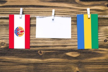 Hanging flags of French Polynesia and Gabon attached to rope with clothes pins with copy space on white note paper on wooden background.Diplomatic relations between countries.