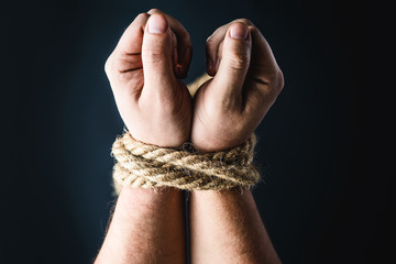 hands tied with rope on black background