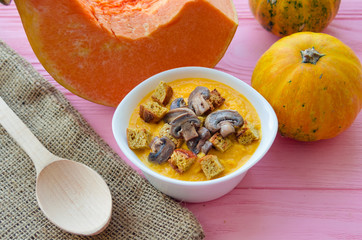 Homemade pumpkin cream soup with mushrooms and croutons, pumpkins on rustic background.