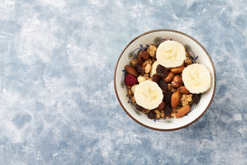 Bowl of granola with nuts, raisins and banana. Concept for a tasty and healthy meal. Rustic wooden background. Copy space.  Top view. 
