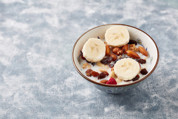 Bowl of granola with milk, nuts, raisins and banana. Concept for a tasty and healthy meal. Rustic wooden background. Copy space. 