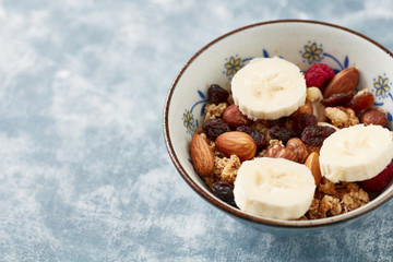 Bowl of granola with nuts, raisins and banana. Concept for a tasty and healthy meal. Rustic wooden background. Copy space. 