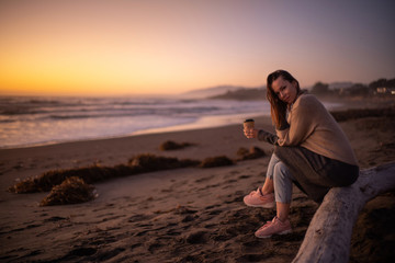 Woman enjoying hot drink on a sunset near ocean