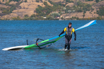 Windsurfer with surfing board and sail coming out from water.