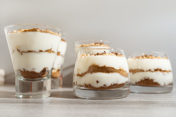 Classic tiramisu dessert in a glass on a gray wooden background. Brightly lit chocolate cake in the amount of three pieces.