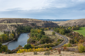 Epic landscape of train tracks cutting through valley alongside a calm river and rolling hills