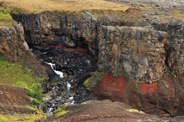 Hengifoss canyon and waterfall, the third highest waterfall in Iceland, surrounded by basaltic strata with red layers of clay between the basaltic layers