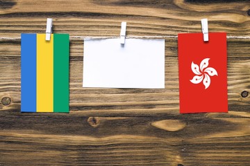 Hanging flags of Gabon and Hong Kong attached to rope with clothes pins with copy space on white...