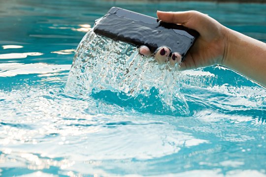 A modern black smartphone makes a splash as it is dropped in the water to test its waterproof construction