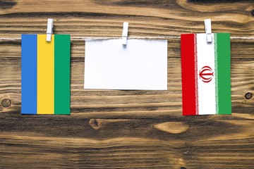 Hanging flags of Gabon and Iran attached to rope with clothes pins with copy space on white note...