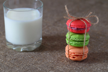 Macarons three pieces red, green and orange tied with rope and glass with milk on burlap tablecloth.