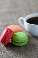 Macarons three pieces red, green, orange and mug with coffee on burlap tablecloth.