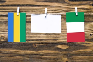Hanging flags of Gabon and Italy attached to rope with clothes pins with copy space on white note...