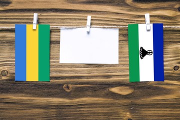 Hanging flags of Gabon and Lesotho attached to rope with clothes pins with copy space on white note...