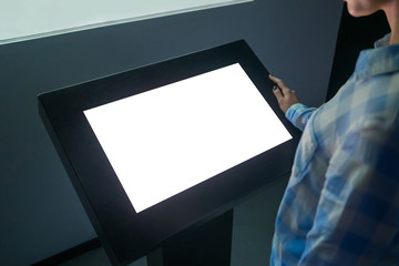 Woman looking at white blank interactive touchscreen display of electronic multimedia kiosk in dark room of technology exhibition - close up view. Mock up, copyspace, template and futuristic concept - obrazy, fototapety, plakaty