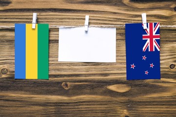 Hanging flags of Gabon and New Zealand attached to rope with clothes pins with copy space on white...