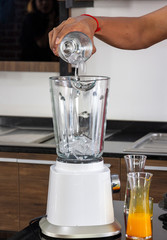 Cropped Image of a man preparing orange juice smoothie. putting ice into a blender in a modern...