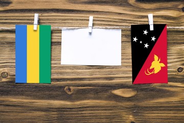 Hanging flags of Gabon and Papua New Guinea attached to rope with clothes pins with copy space on...