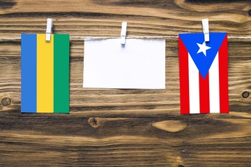 Hanging flags of Gabon and Puerto Rico attached to rope with clothes pins with copy space on white...
