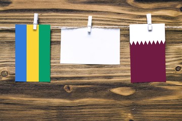 Hanging flags of Gabon and Qatar attached to rope with clothes pins with copy space on white note...