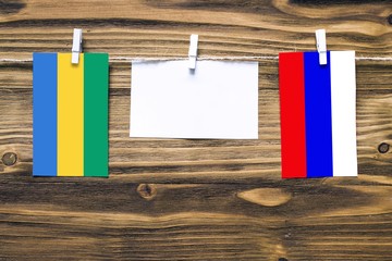 Hanging flags of Gabon and Russia attached to rope with clothes pins with copy space on white note paper on wooden background.Diplomatic relations between countries.