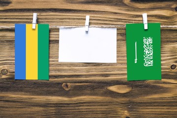 Hanging flags of Gabon and Saudi Arabia attached to rope with clothes pins with copy space on white...