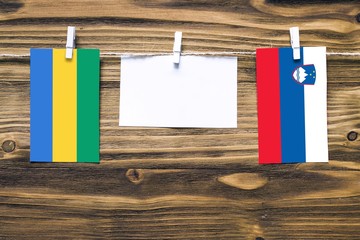 Hanging flags of Gabon and Slovenia attached to rope with clothes pins with copy space on white...