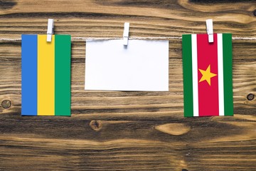 Hanging flags of Gabon and Suriname attached to rope with clothes pins with copy space on white...