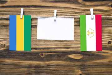 Hanging flags of Gabon and Tajikistan attached to rope with clothes pins with copy space on white...