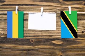 Hanging flags of Gabon and Tanzania attached to rope with clothes pins with copy space on white...