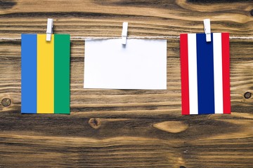 Hanging flags of Gabon and Thailand attached to rope with clothes pins with copy space on white...