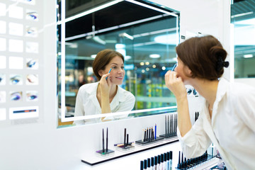 Young beautiful girl paint her eyes with a blue pencil in front of big mirror