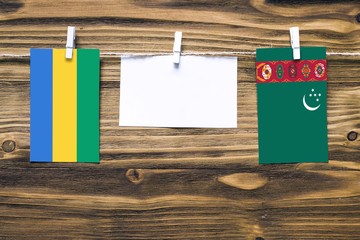 Hanging flags of Gabon and Turkmenistan attached to rope with clothes pins with copy space on white...