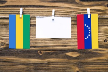 Hanging flags of Gabon and Venezuela attached to rope with clothes pins with copy space on white...