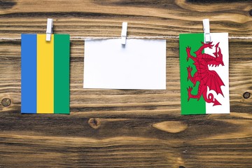 Hanging flags of Gabon and Wales attached to rope with clothes pins with copy space on white note...