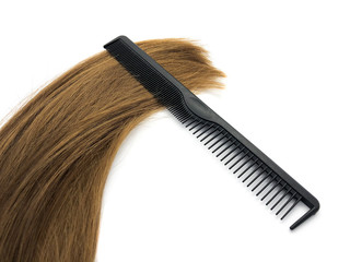 Barber comb and hair isolated on a white background. Composition of black comb and brown hair. Professional hairbrush. Women's hair. Set for a beauty salon