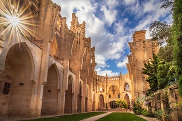 Fototapeta premium Esgesia Nova Spanish church without roof, entrnce of palm trees leading into garden, sunny day with blue sky and white clouds, Son Servera, Mallorca, Spain