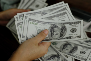 Hand holding smartphone and calculator on a stack of 100 US dollars banknotes