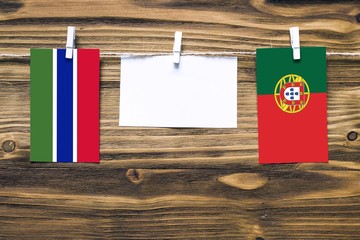 Hanging flags of Gambia and Portugal attached to rope with clothes pins with copy space on white note paper on wooden background.Diplomatic relations between countries.
