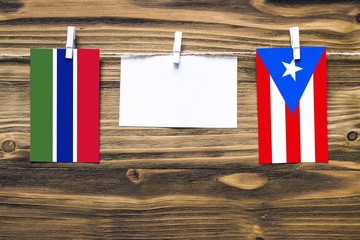 Hanging flags of Gambia and Puerto Rico attached to rope with clothes pins with copy space on white note paper on wooden background.Diplomatic relations between countries.