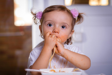 Fototapeta premium Adorable little girl eating spaghetti with Bolognese sauce with her hands. Infant feeding