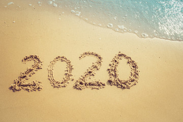 Happy New Year 2020 concept, 2020 number lettering on the sea beach, wave and golden light of sunset.