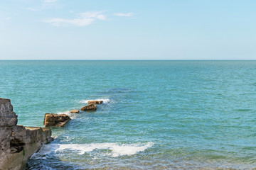 Blue sea with blue sky and rocks reaching to horizon