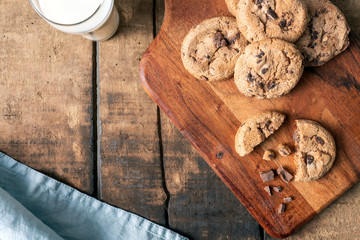 Chocolate chip cookies on wooden cutting board and rustic background with milk mug and milk glass....