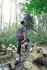Tired woodcutter after hard work in forest with chainsaw. Lumberjack cutting down birch tree with chainsaw.