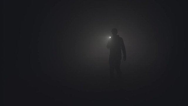 Silhouette of man in thick fog. Stock footage. Black silhouette of man with flashlight shining in thick grey smoke. Man with flashlight makes his way through darkness in smoke