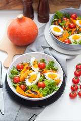 Lunch bowl with cherry tomatoes, roasted pumpkin, green salad, seeds and boiled eggs. Grey plate on white background. 