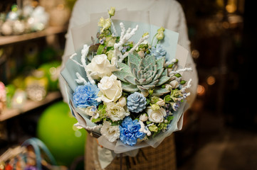 Woman holding a bouquet of white roses, blue carnation, artificial branches and glittered succulent