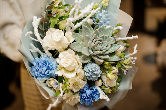 Girl holding a bouquet of white roses, blue carnation, artificial branches and glittered succulent